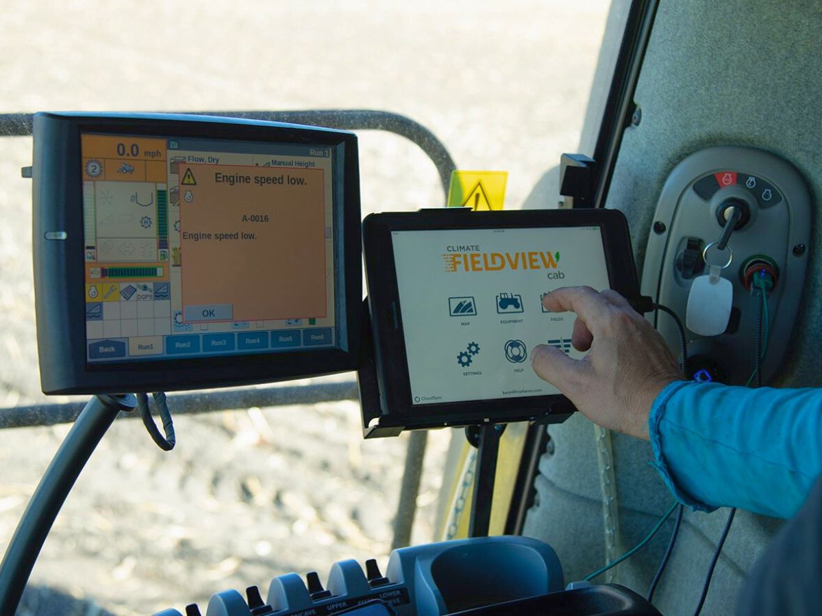 Person operating farming equipment with digital screens displaying agricultural data.