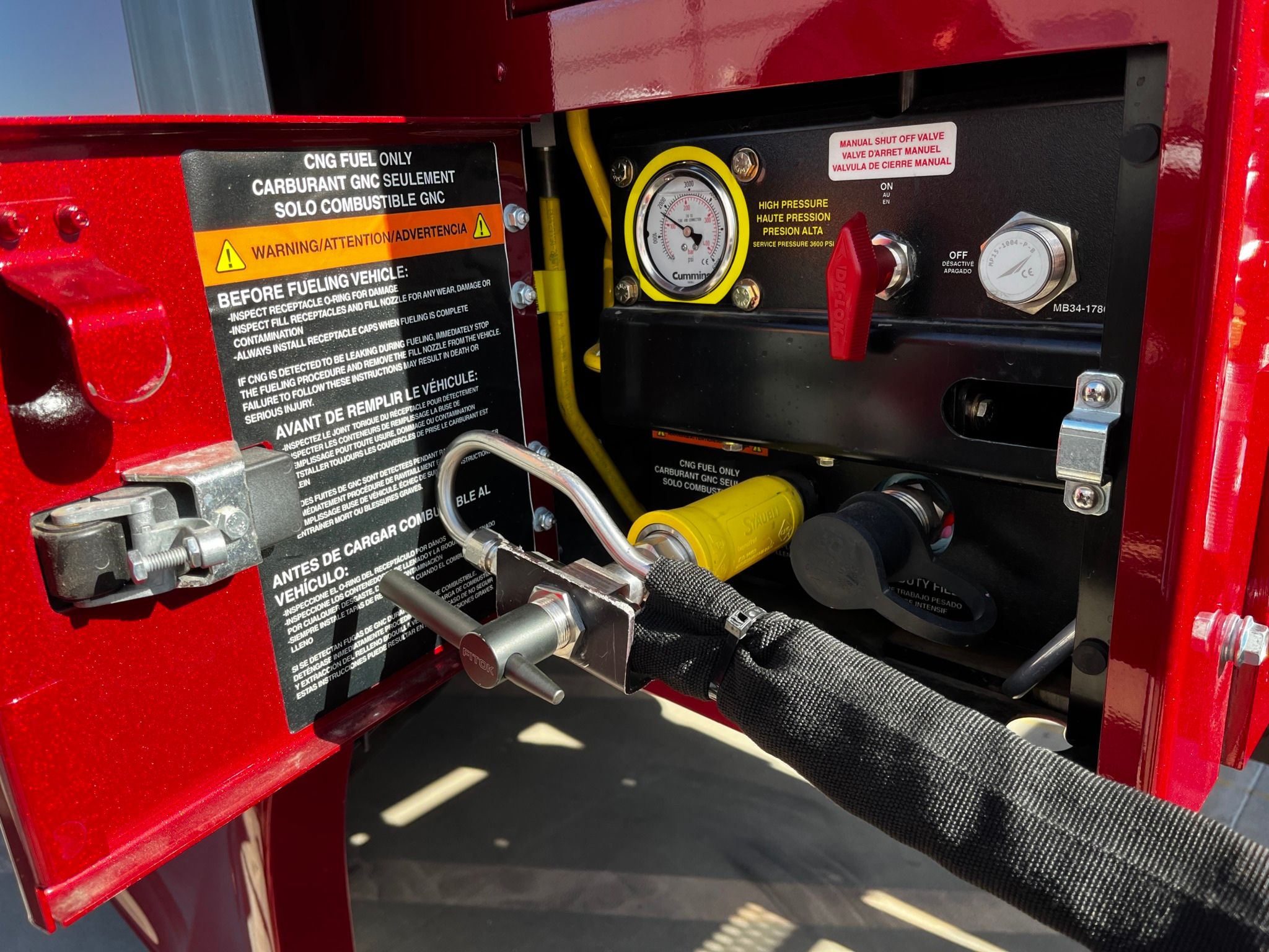 Close-up of a CNG fuel compartment with gauges, red and yellow controls, and warning labels on a red vehicle.